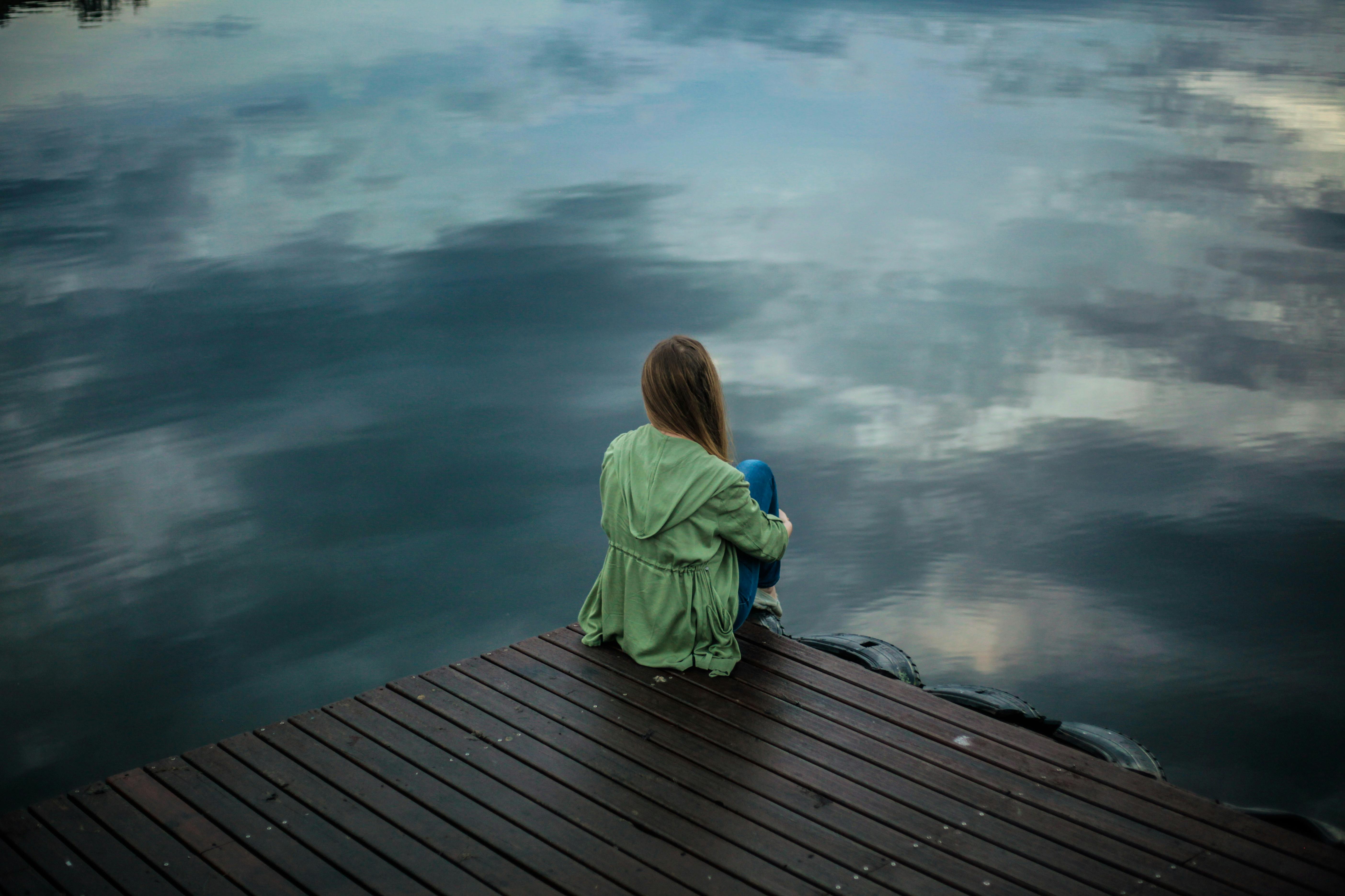 a woman sat on a dock looking out into the water