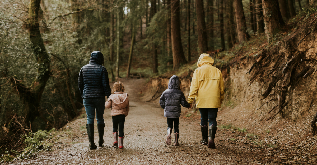 two adults and two children walking through a forest wearing coats and boots