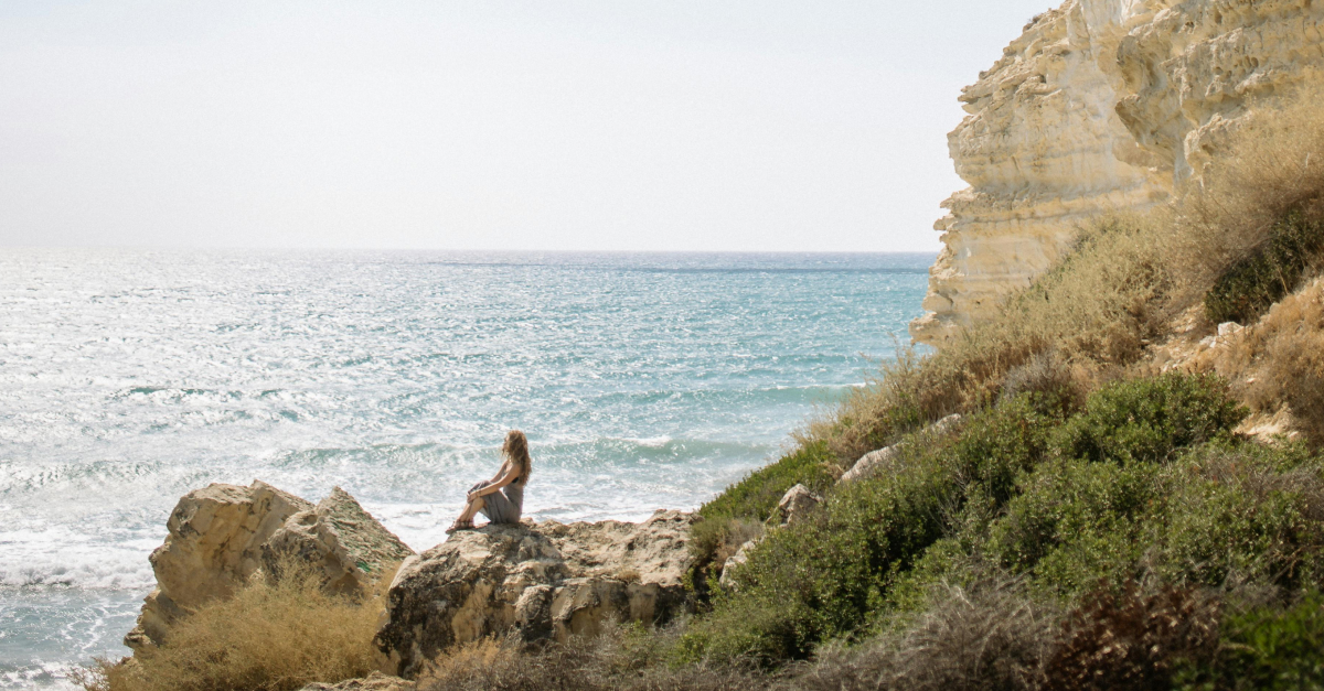woman sat on rock looking at the ocean
