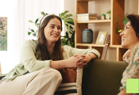 Two women sat on the couch looking happy